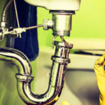 a sink drain is visible, broken with water running onto the floor, a concerned woman is on the phone calling a plumbing contractor